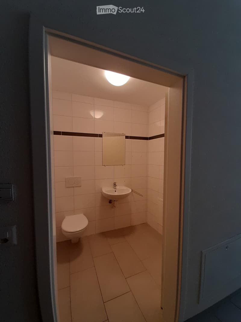 Small bathroom with white tiled walls and floor, featuring a toilet, sink, and mirror.