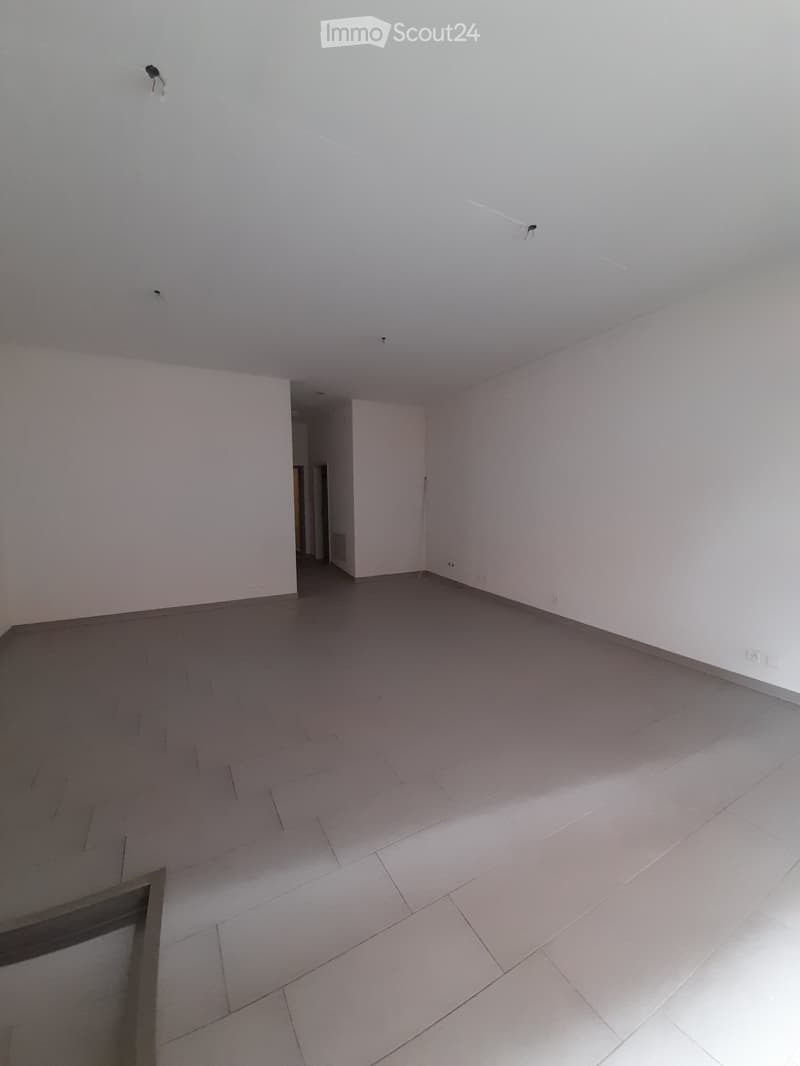 Empty room with white walls and grey tiled floor, featuring a doorway leading to another space.