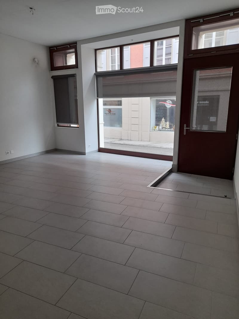 Empty room with tiled floor, large windows, and a glass door leading outside. No furniture or equipment visible.