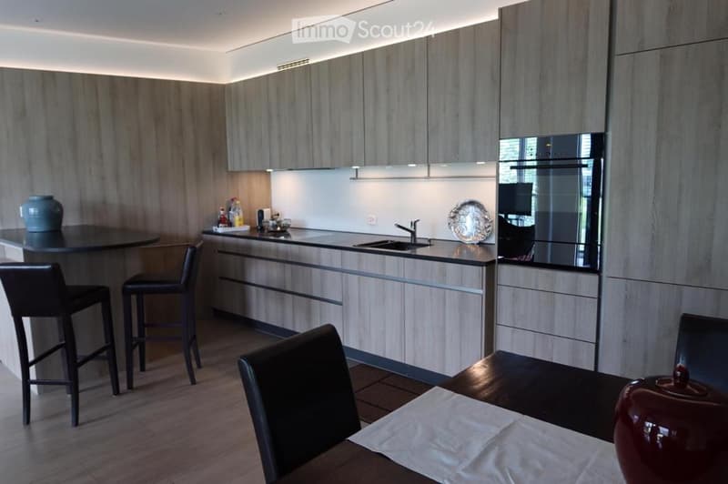 Modern kitchen with light wood cabinets, stainless steel appliances, bar stools, dining table, and decorative items.