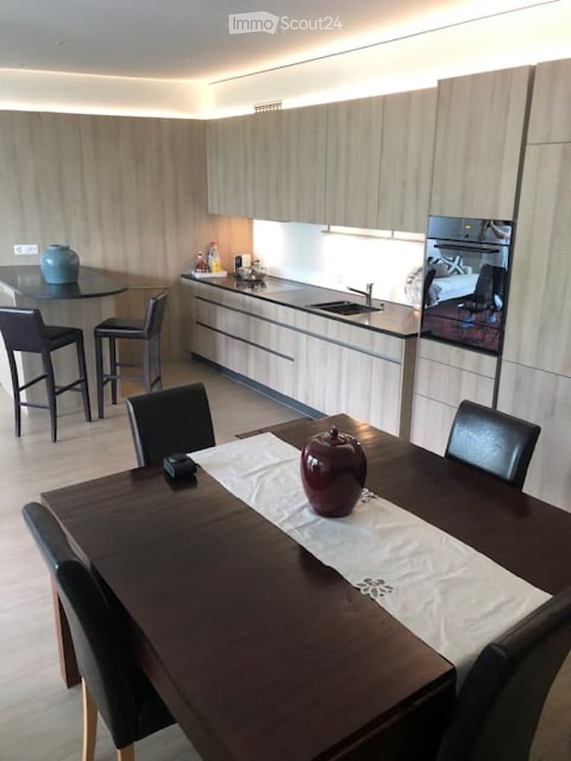 Modern kitchen and dining area with light wood cabinets, stainless steel appliances, a round dining table with chairs, and bar stools near the counter.