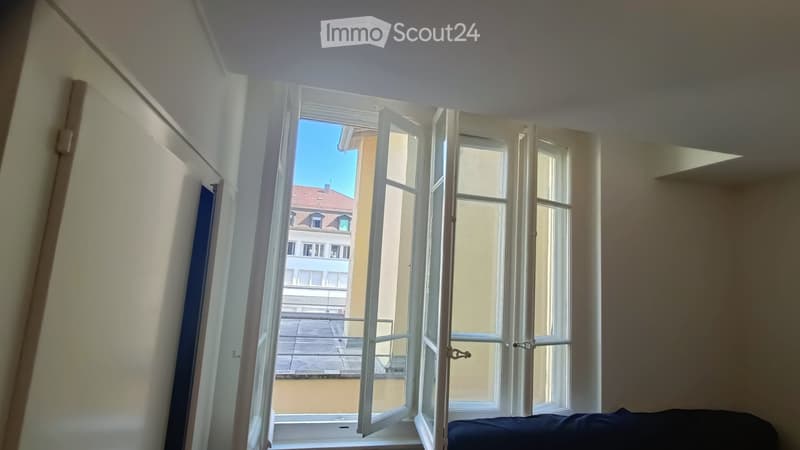 Empty room with large open windows offering a view of the city and a balcony area. No furniture or furnishings are present.