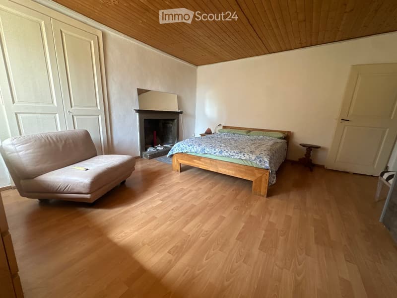 Cozy bedroom with wooden flooring, a fireplace, a sofa, a bed with a patterned duvet, and a nightstand.