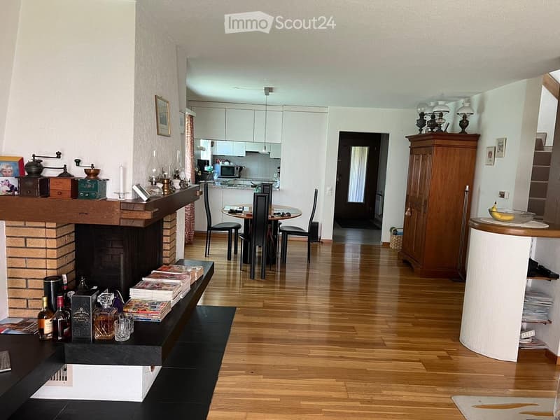 Open-plan living and dining area with a fireplace, wooden flooring, and modern kitchen in the background.