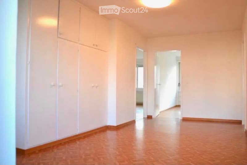 Empty hallway with light-colored walls, wooden flooring, and built-in white cabinets on one side. The hallway leads to an open doorway at the end.