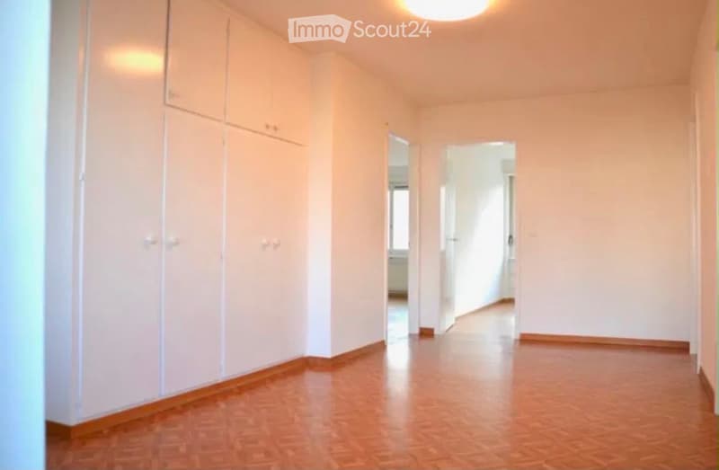 Empty hallway with light-colored walls, wooden flooring, and built-in white cabinets on one side. Two open doorways lead to other rooms.