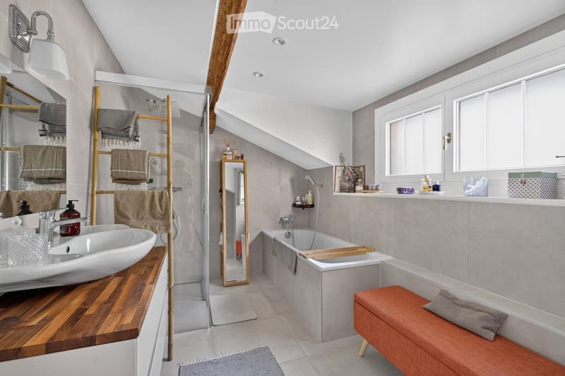 Modern bathroom with a white sink, bathtub, wooden stool, mirror, towel rack, and shelves. The space features large windows and a sleek design with neutral tones.