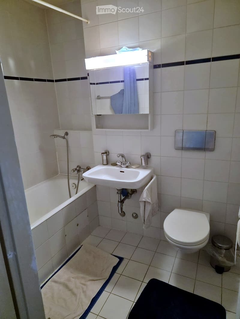 A small bathroom with a bathtub, sink, toilet, mirror, and towels.