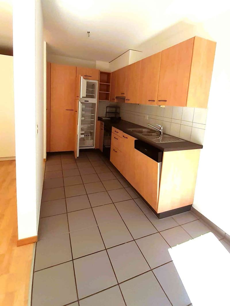 Modern kitchen with light wooden cabinets, tiled floor, and stainless steel sink.