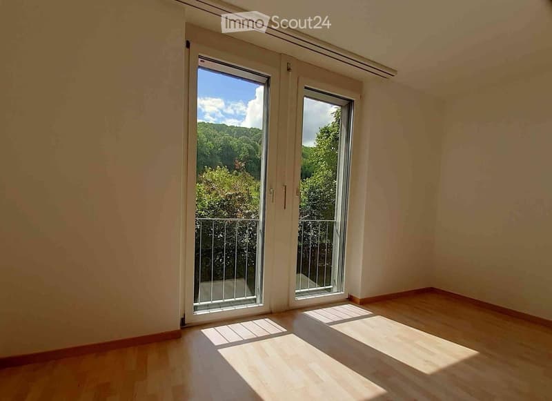 Empty room with wooden flooring, large sliding glass doors leading to a balcony, and natural light streaming in.