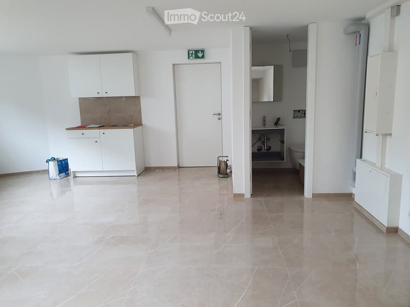 Empty room with white cabinets, a sink, and a door leading to a small bathroom area. The space features tiled flooring and white walls.