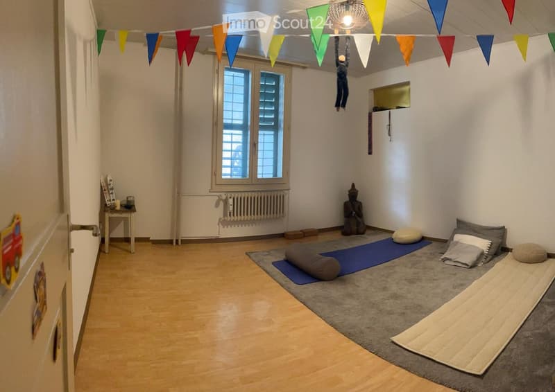 Minimalist room with wooden flooring, large windows, yoga mat, pillows, and a small table with a candle.
