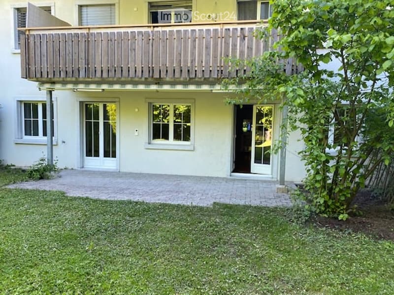 Two-story building with a balcony, white walls, large windows, and a small garden area.