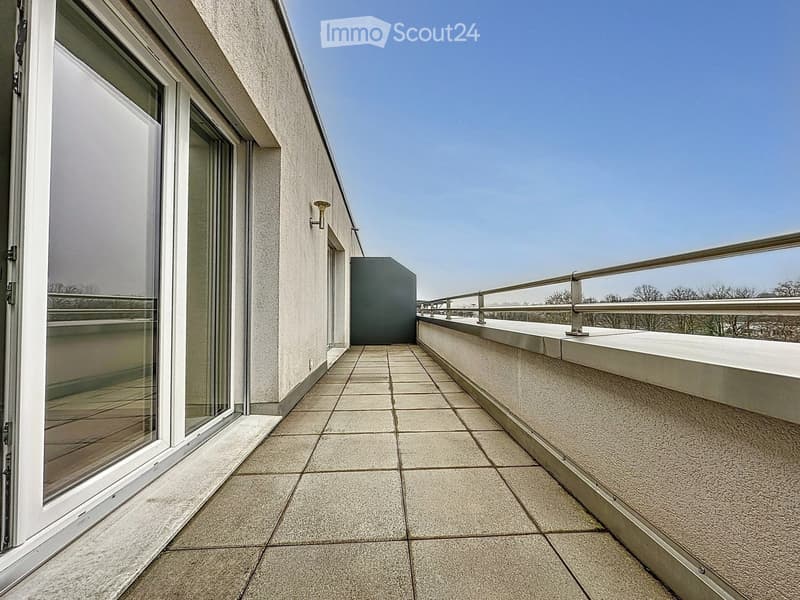 Modern rooftop terrace with tiled flooring, glass sliding doors, metal railing, and a clear blue sky view.