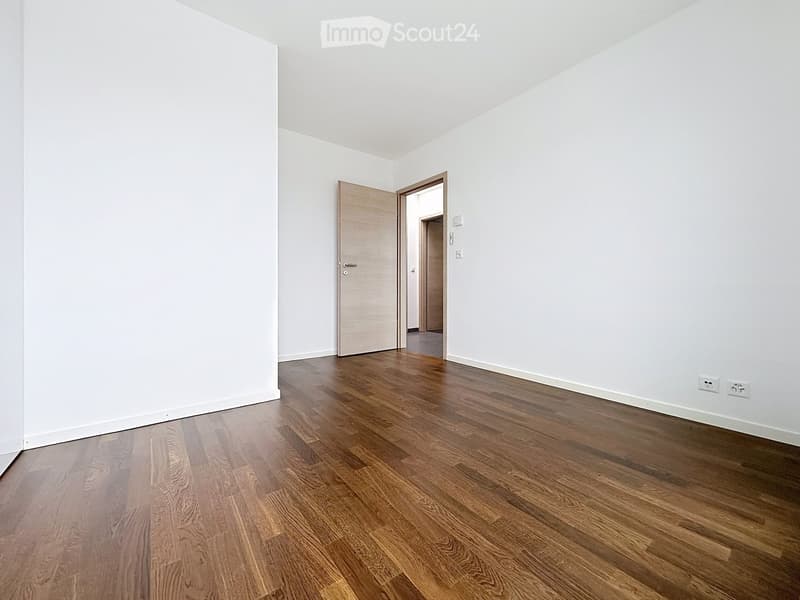 Empty room with white walls and wooden flooring, featuring a single door leading to another space.