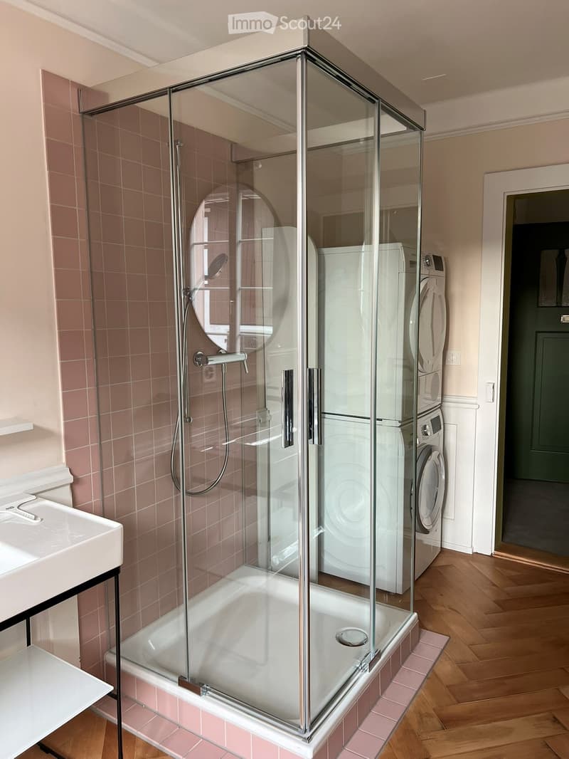 Modern bathroom with a glass-enclosed shower, bathtub, sink, and stacked washing machine and dryer unit.