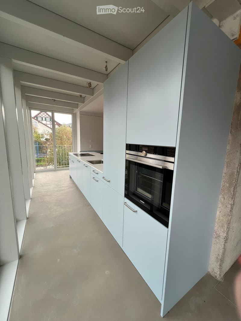Modern kitchen with white cabinets, a sink, and an oven, featuring a large window with a view of the outside.