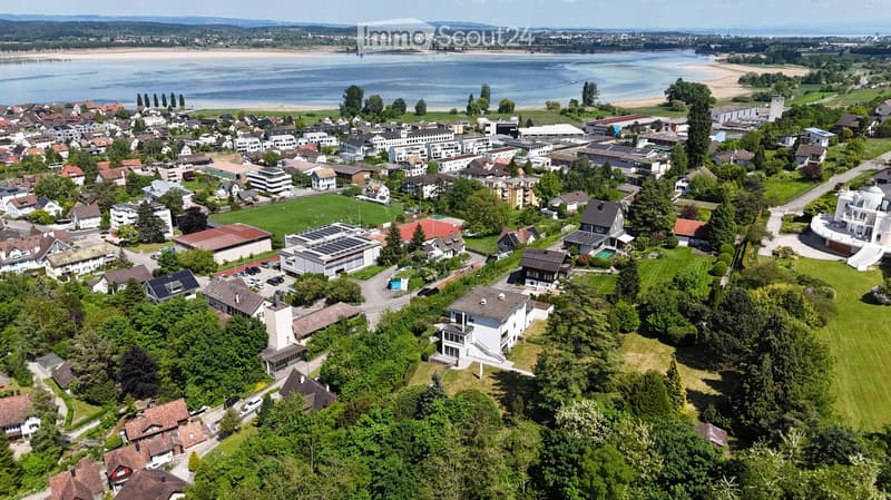 Aerial view of a suburban town with houses, green spaces, and a body of water in the background.