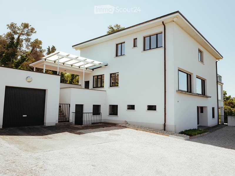 Modern two-story white house with large windows, garage, and covered patio area.