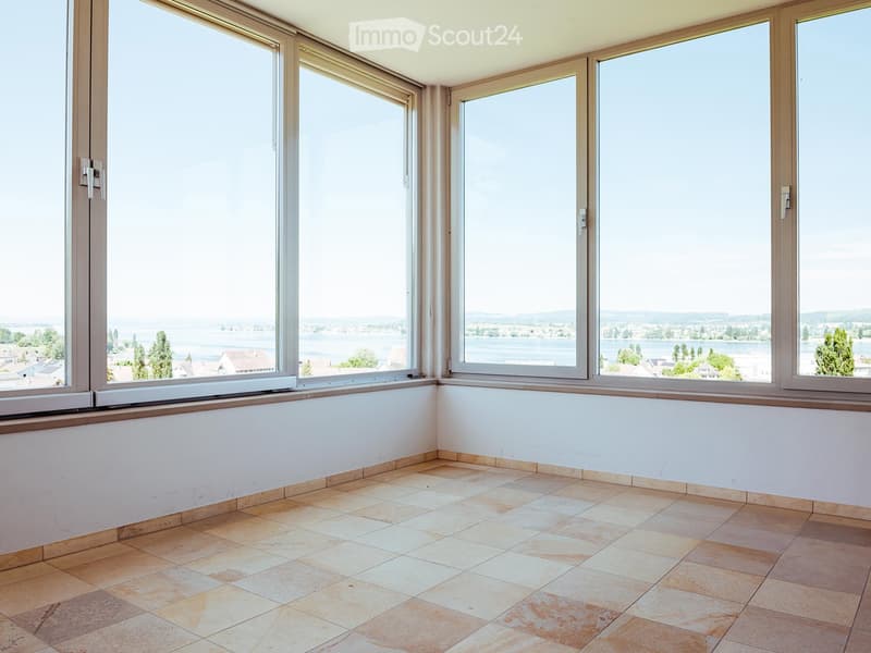Empty room with large windows offering a scenic view, tiled floor, and white walls.