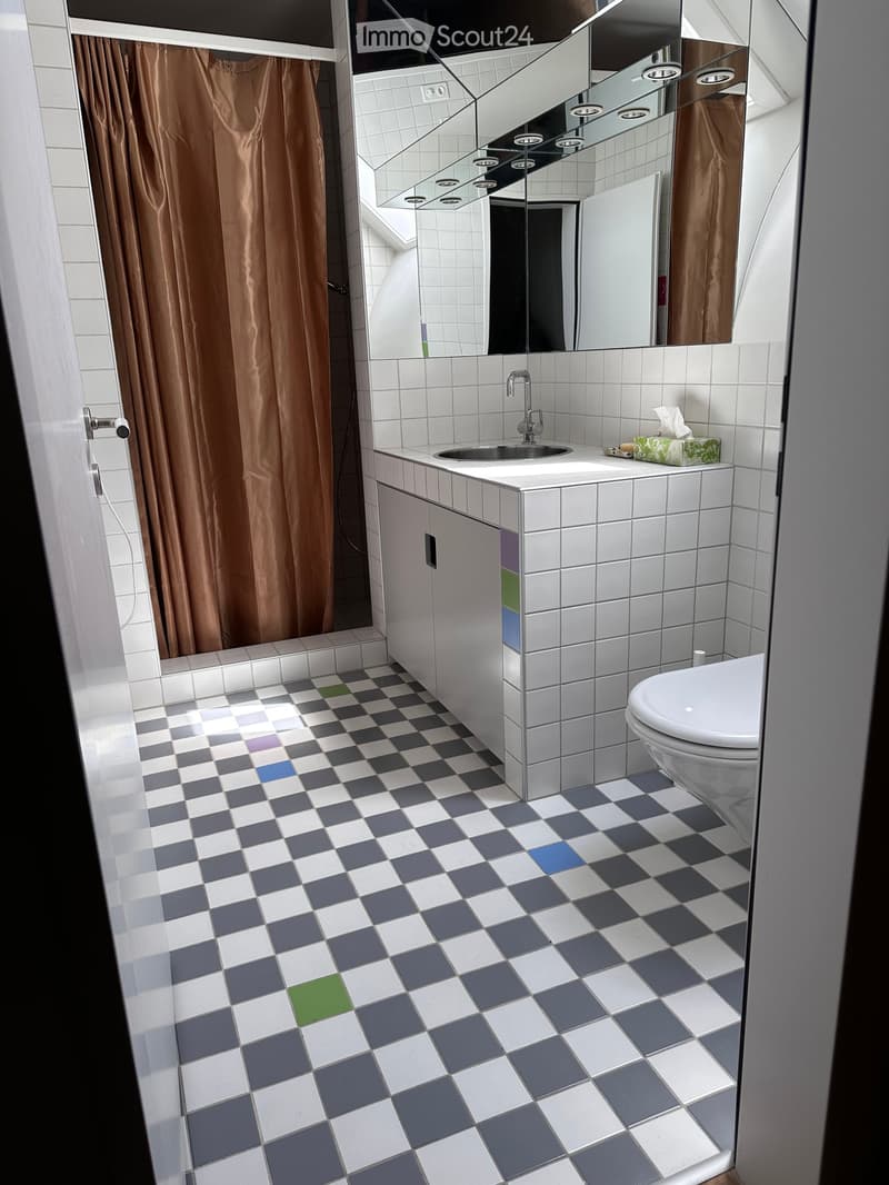 Modern bathroom with white tiled walls, a large mirror, a sink with a chrome faucet, a toilet, and a colorful checkered floor.