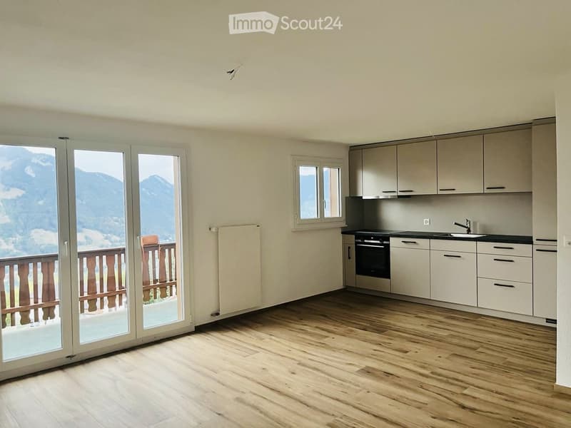 Modern kitchen with light-colored cabinets, wooden flooring, and large windows offering a scenic mountain view.