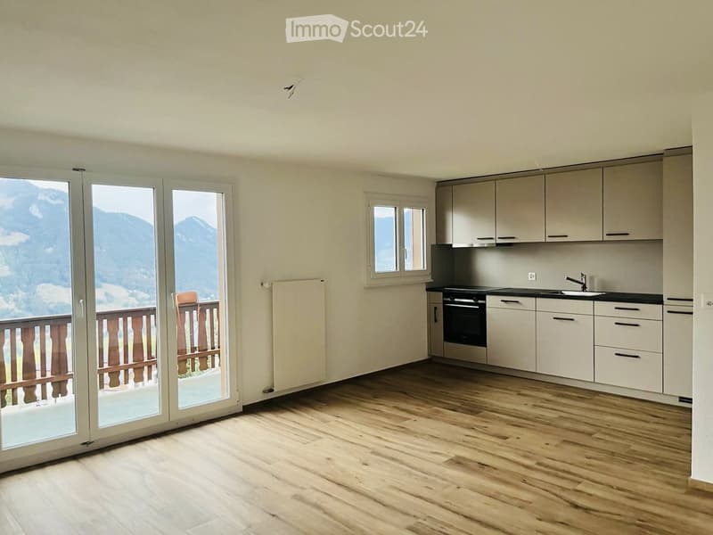 Modern kitchen with light-colored cabinets, wooden flooring, and large windows offering a scenic mountain view.