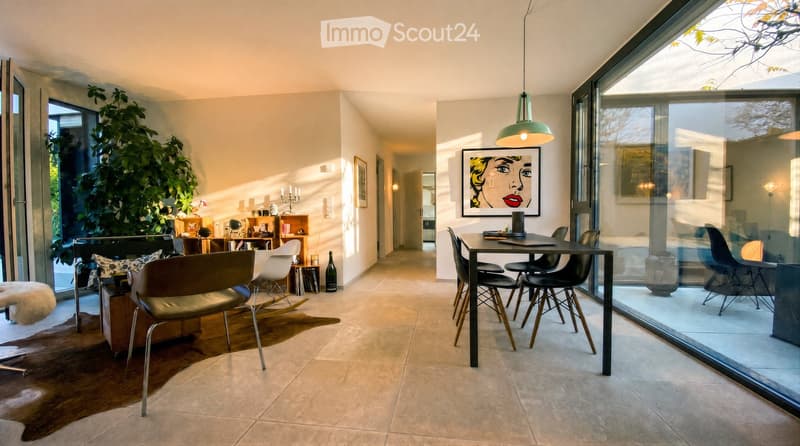 Modern living and dining area with large windows, a sofa, chairs, a dining table, pendant light, and artwork.
