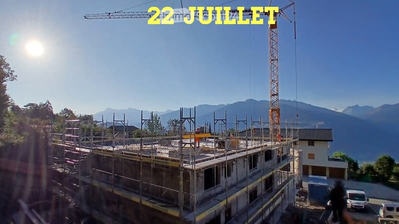 A multi-story building under construction with scaffolding, a crane, and a clear view of mountains in the background.