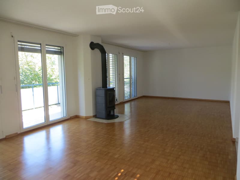 Empty room with wooden flooring, white walls, large sliding glass doors leading to a balcony, and a modern wood-burning stove with a chimney.