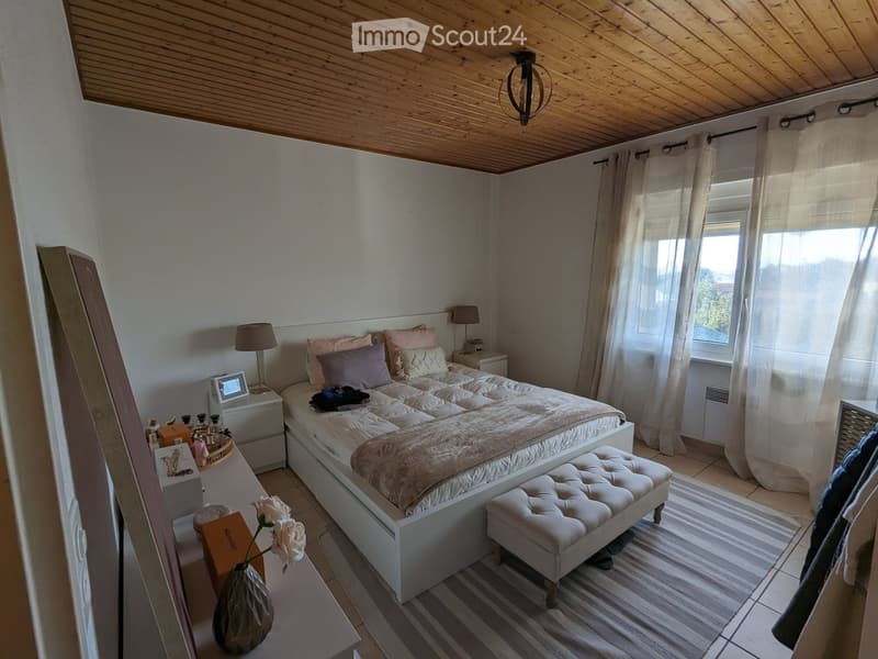 Cozy bedroom with a large bed, nightstands, lamps, a small stool, and a vase with flowers on a table.