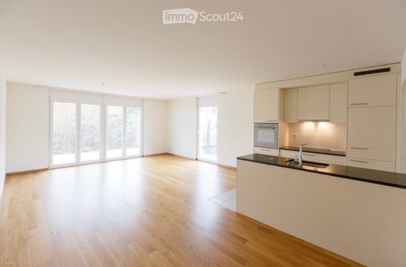 Open-plan kitchen and living space with light wood flooring, white cabinetry, and large glass doors leading to an outdoor area.