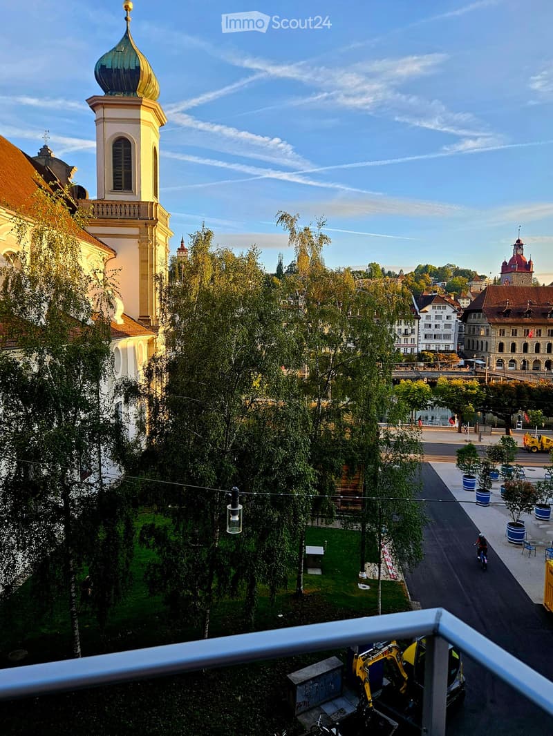 Balcony overlooking a city square with historic buildings, trees, and a small park area.