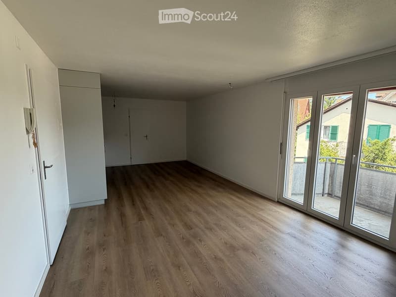 Empty room with light wooden flooring, white walls, and large sliding glass doors leading to a balcony.