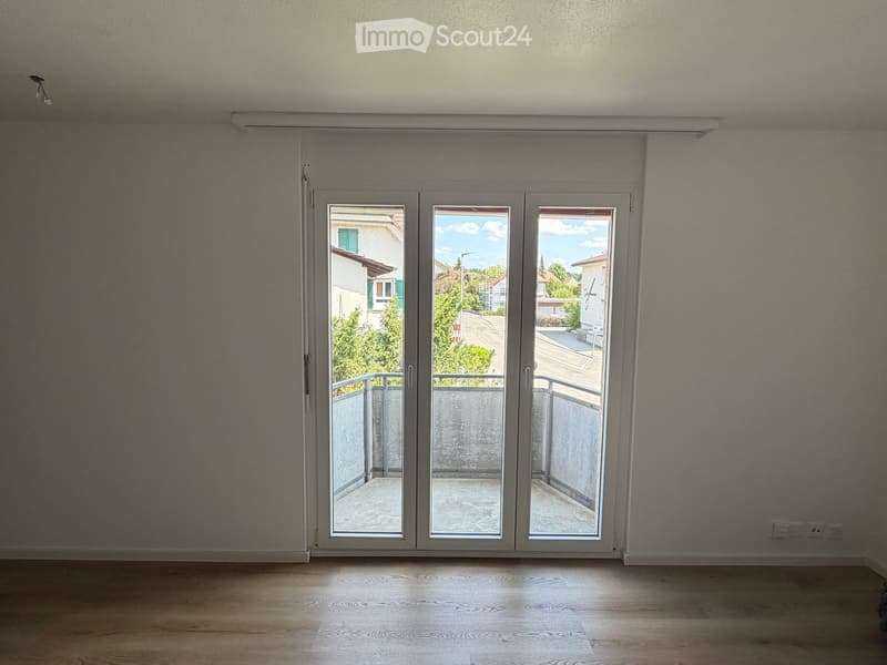 Empty room with wooden flooring, large sliding glass doors leading to a balcony, and neutral-colored walls.
