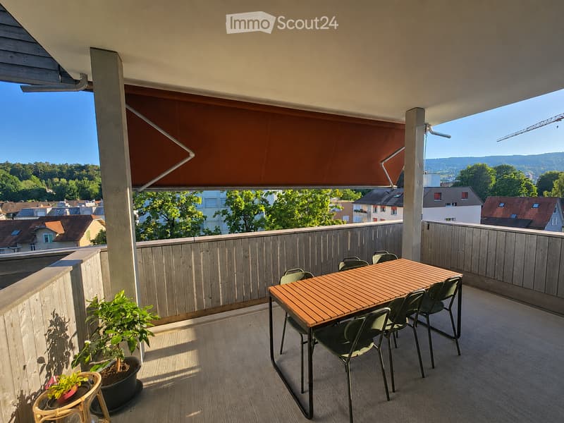 Balcony with wooden decking, a table and chairs, potted plants, and a view of the city and surrounding landscape.
