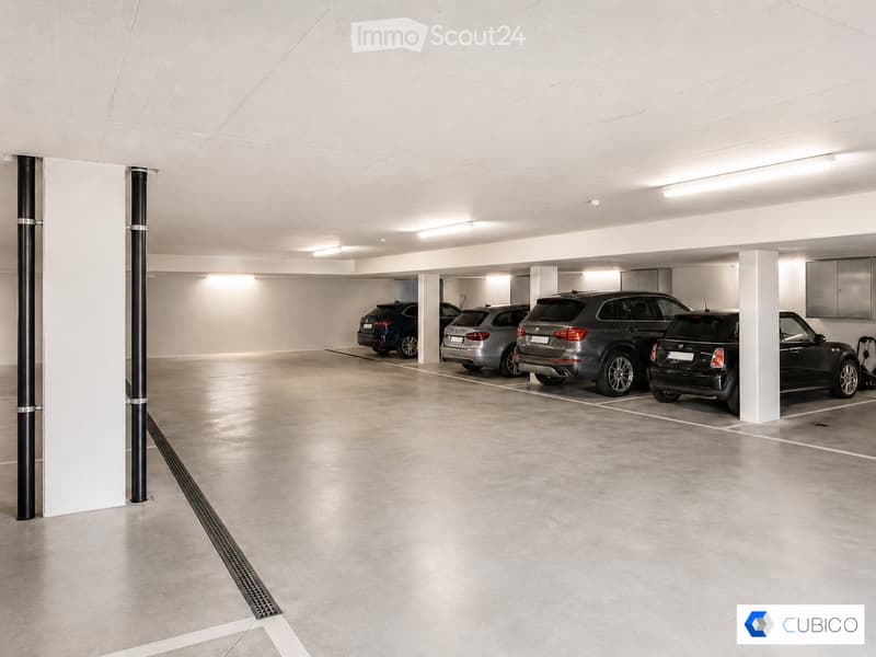Underground parking area with several parked cars, white walls, and a clean, organized space.
