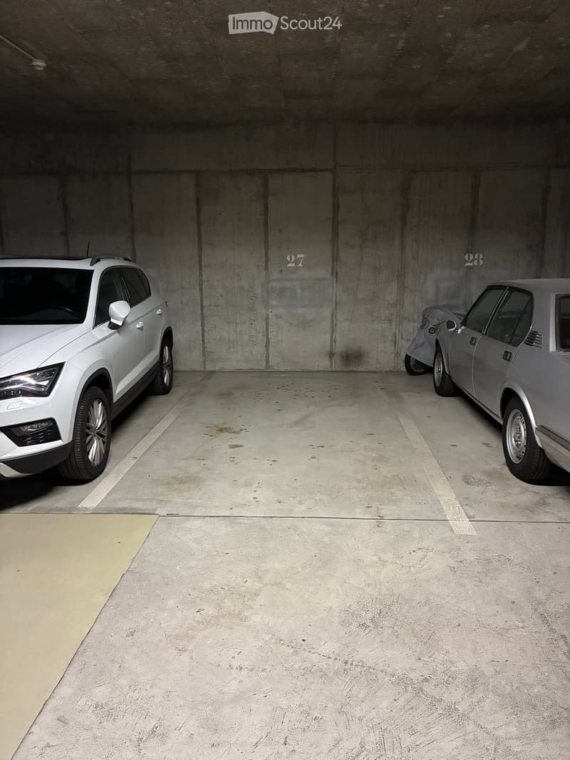 Underground parking area with two parked cars, marked parking spaces numbered 27 and 28, and a concrete floor.