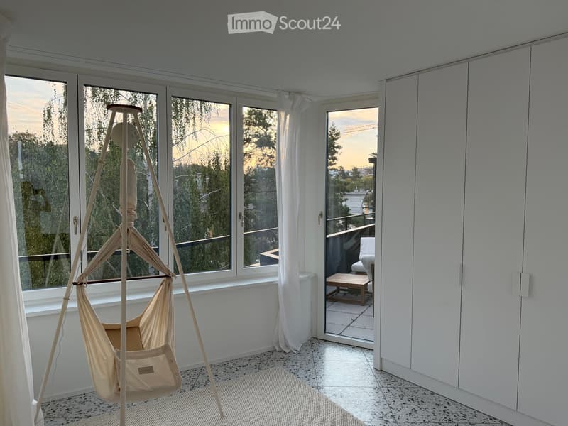 Bright room with large windows and sliding glass doors leading to a balcony. Features a hanging hammock and built-in white cabinetry.