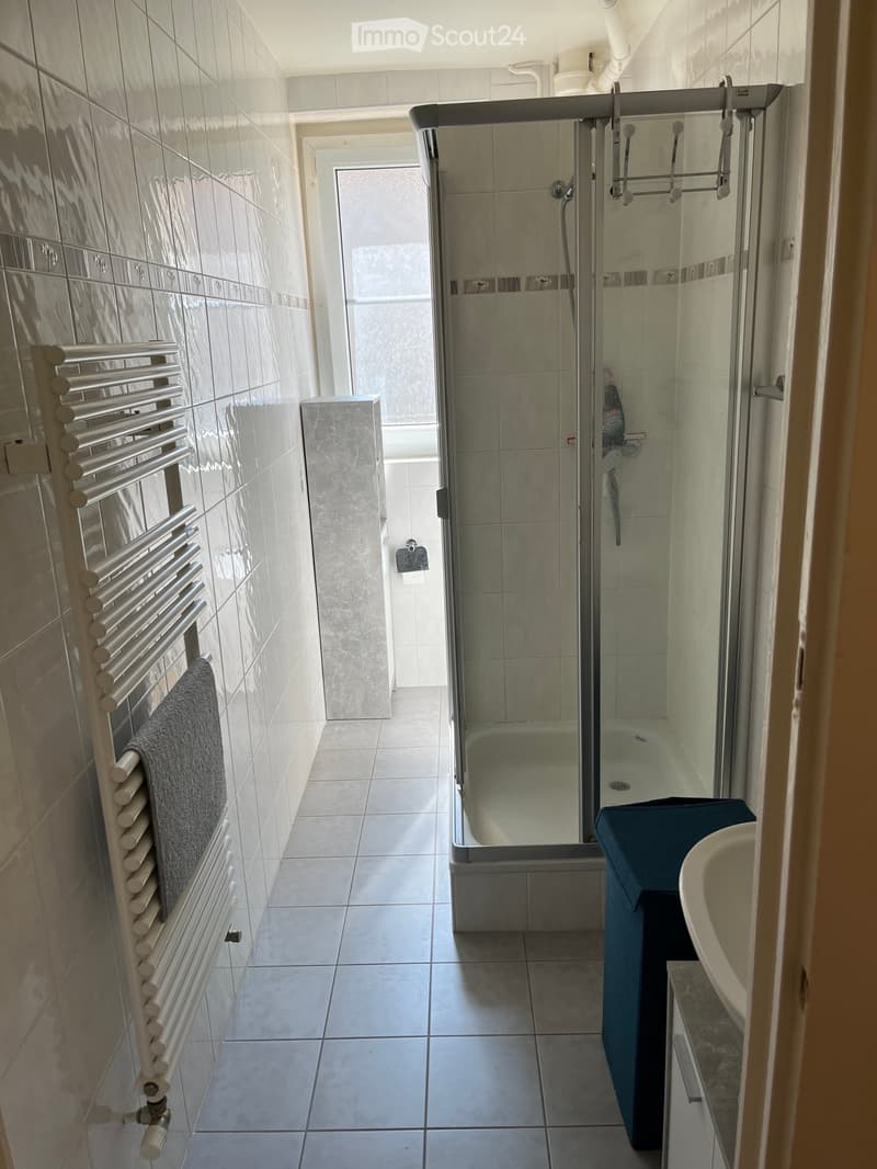 Modern bathroom with a glass-enclosed shower, a sink with a blue cabinet, a towel on a radiator, and tiled walls and floor.