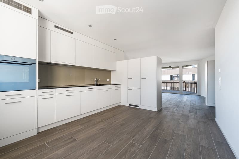 Modern kitchen with white cabinets, dark countertops, and wooden flooring. Features a sink with a modern faucet and built-in appliances.