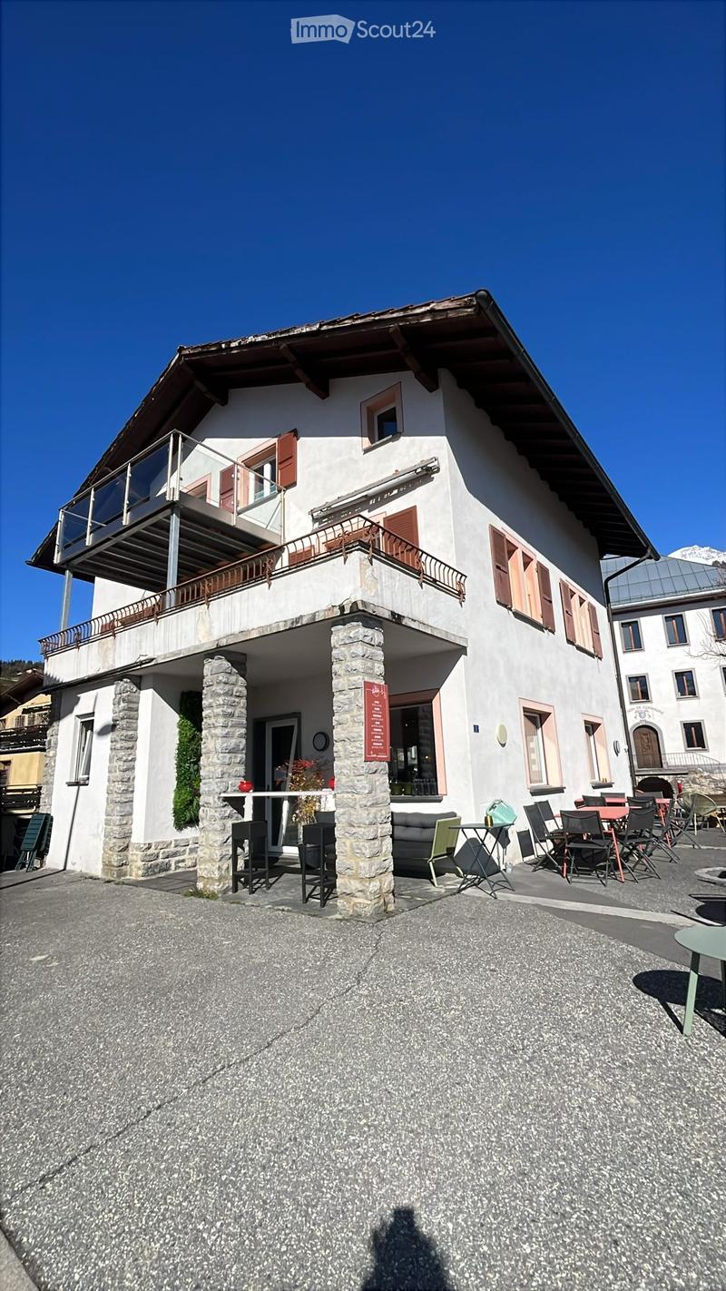 Two-story building with a balcony, stone pillars, and outdoor seating area with tables and chairs.