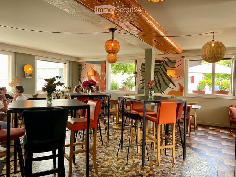 Modern restaurant interior with colorful seating, patterned tile floor, large windows, and decorative vases on tables.