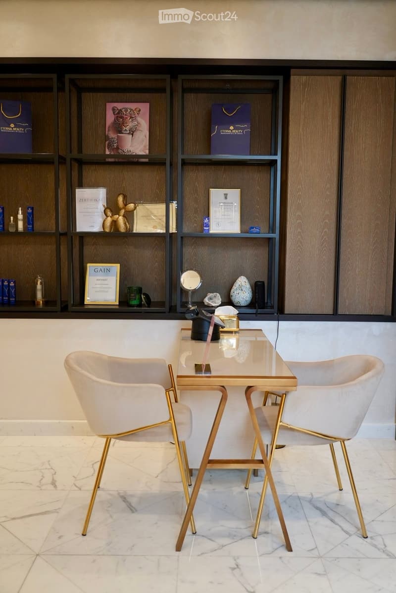 A modern, well-furnished room with a glass table, two elegant chairs, and wooden shelves displaying various decorative items and certificates.