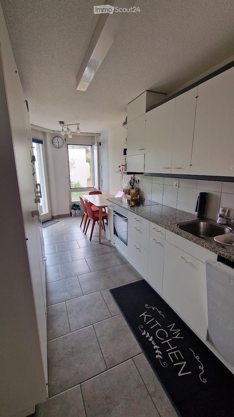 Modern kitchen with white cabinets, granite countertop, stainless steel sink, dishwasher, and a small dining area with a table and chairs.
