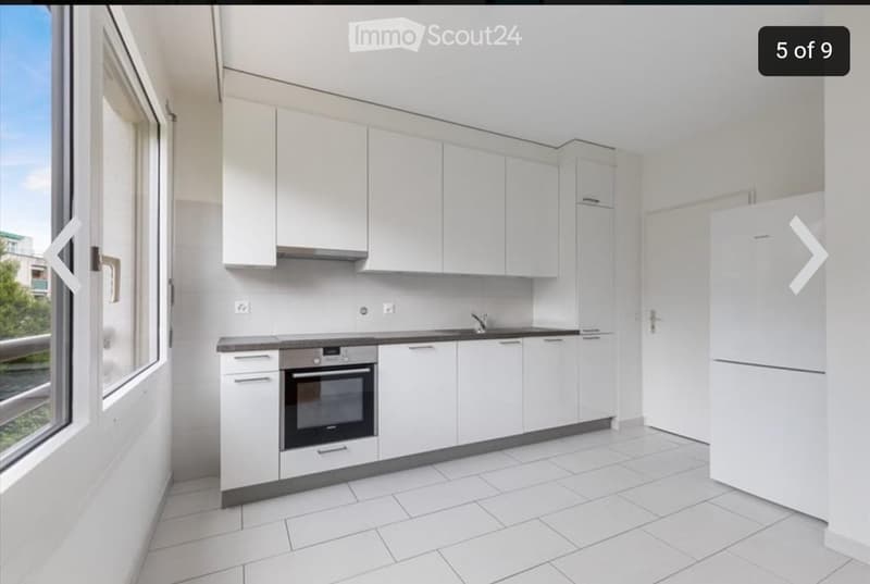 Modern kitchen with white cabinets, a built-in oven, a refrigerator, and a sink with a faucet. The space features white tiled flooring and large windows offering natural light.