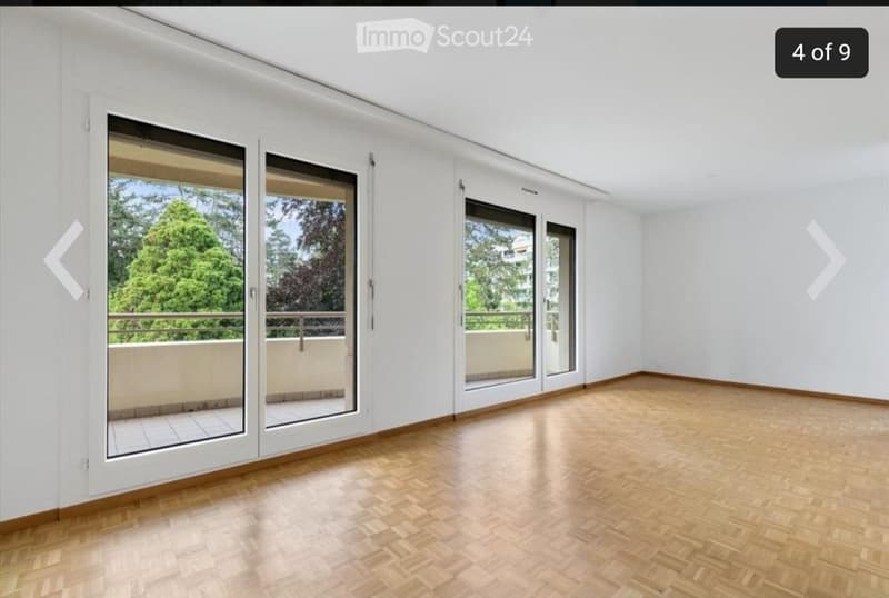 Empty room with wooden flooring, white walls, and large sliding glass doors leading to a balcony with a view of greenery.