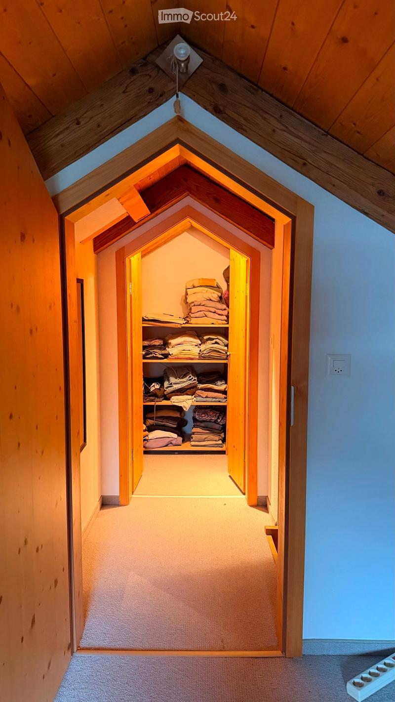 A narrow hallway with wooden walls and a slanted ceiling, leading to an open closet with neatly stacked towels and linens on shelves.