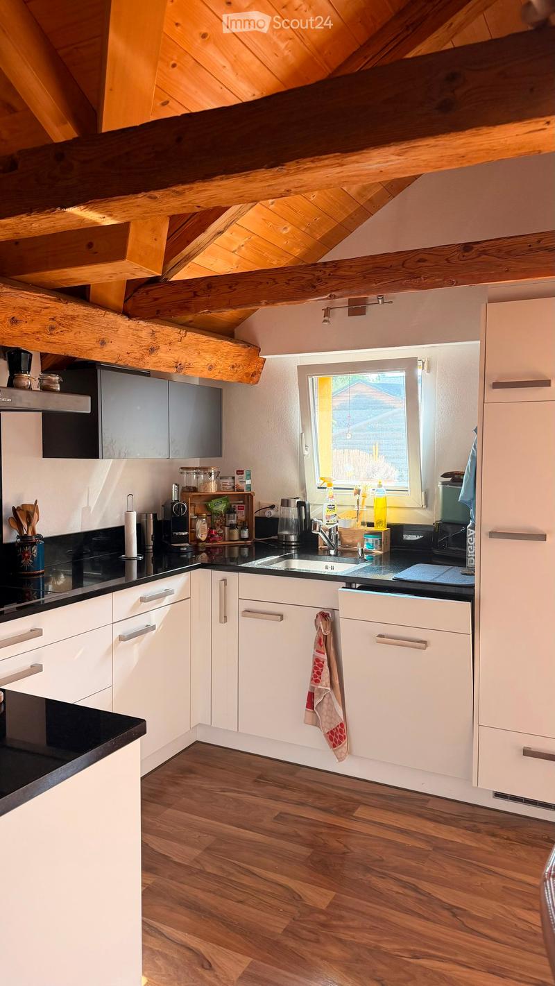 Modern kitchen with white cabinets, wooden floor, black countertops, and stainless steel appliances. Features a window with a view of the garden, various kitchen utensils, and a coffee maker on the counter.