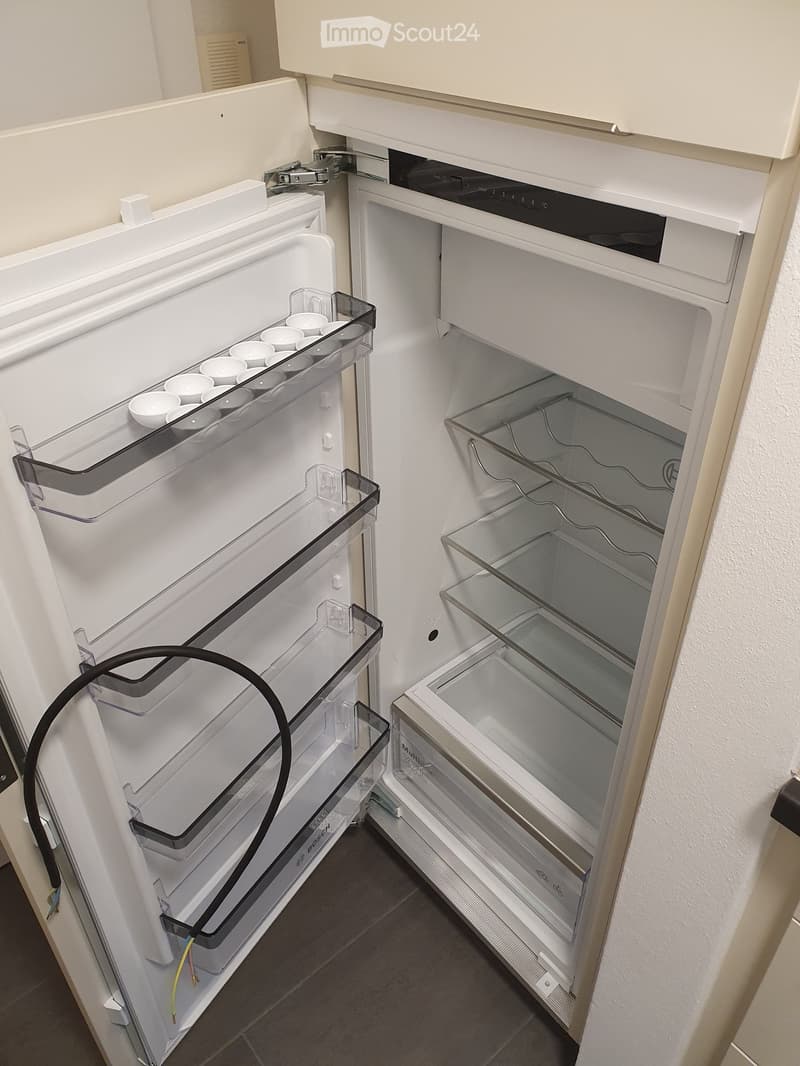 Open refrigerator with multiple compartments and shelves, featuring a modern design with transparent glass shelves and a sleek white finish.